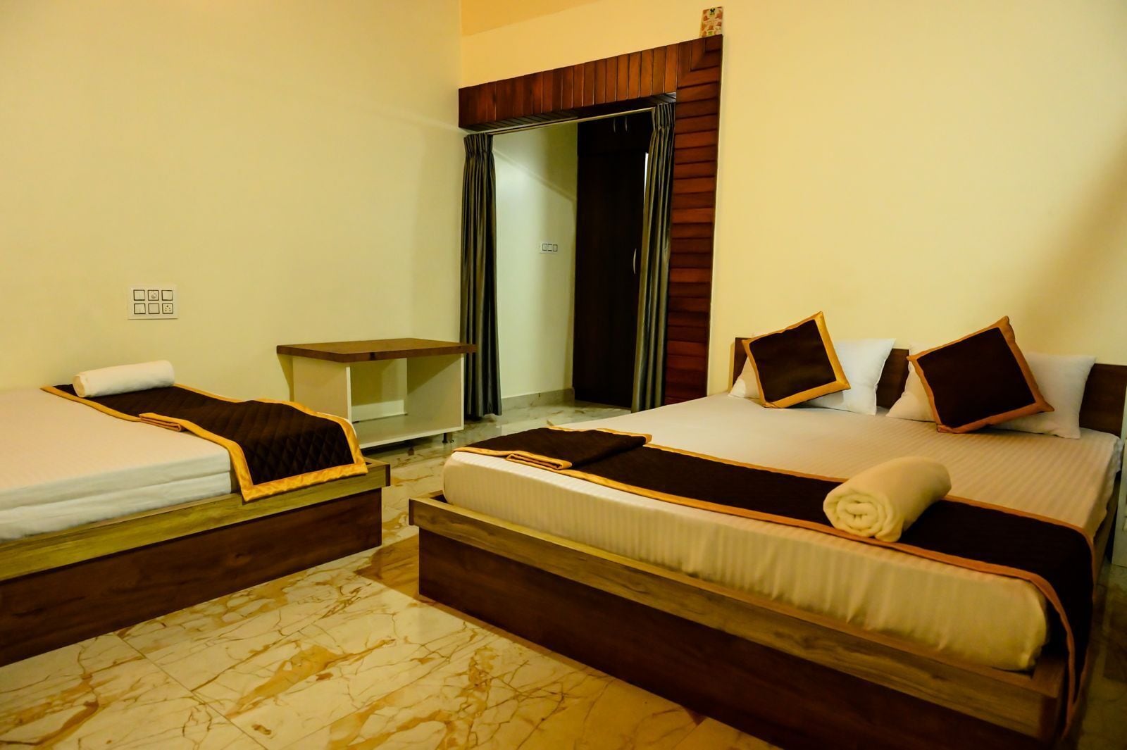 A hotel room with two single beds, a large bed, a wooden nightstand, and a wardrobe.