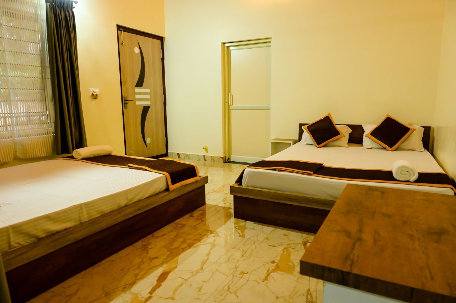 A hotel room with two beds, a wooden headboard, a marble floor, and a door with a mirror.