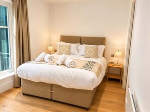 A neatly made bed with white linens, two bedside lamps, and a window with curtains.