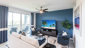 Ein modernes Wohnzimmer mit einer Couch, einem Couchtisch, einem Fernseher und einem Balkon mit Gartenmöbeln.