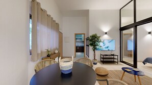 A modern living room with a dining area, a kitchen in the background, and a large TV mounted on the wall. - Apartment 0 Bedrooms MFA, 400m Praia dos Pescadores (Albufeira)