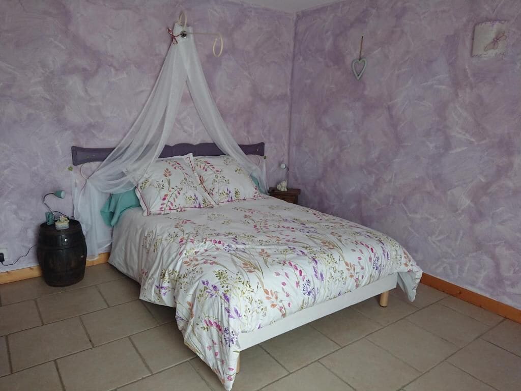 Un dormitorio con cama, mesita de noche, calentador en la pared y cortina.