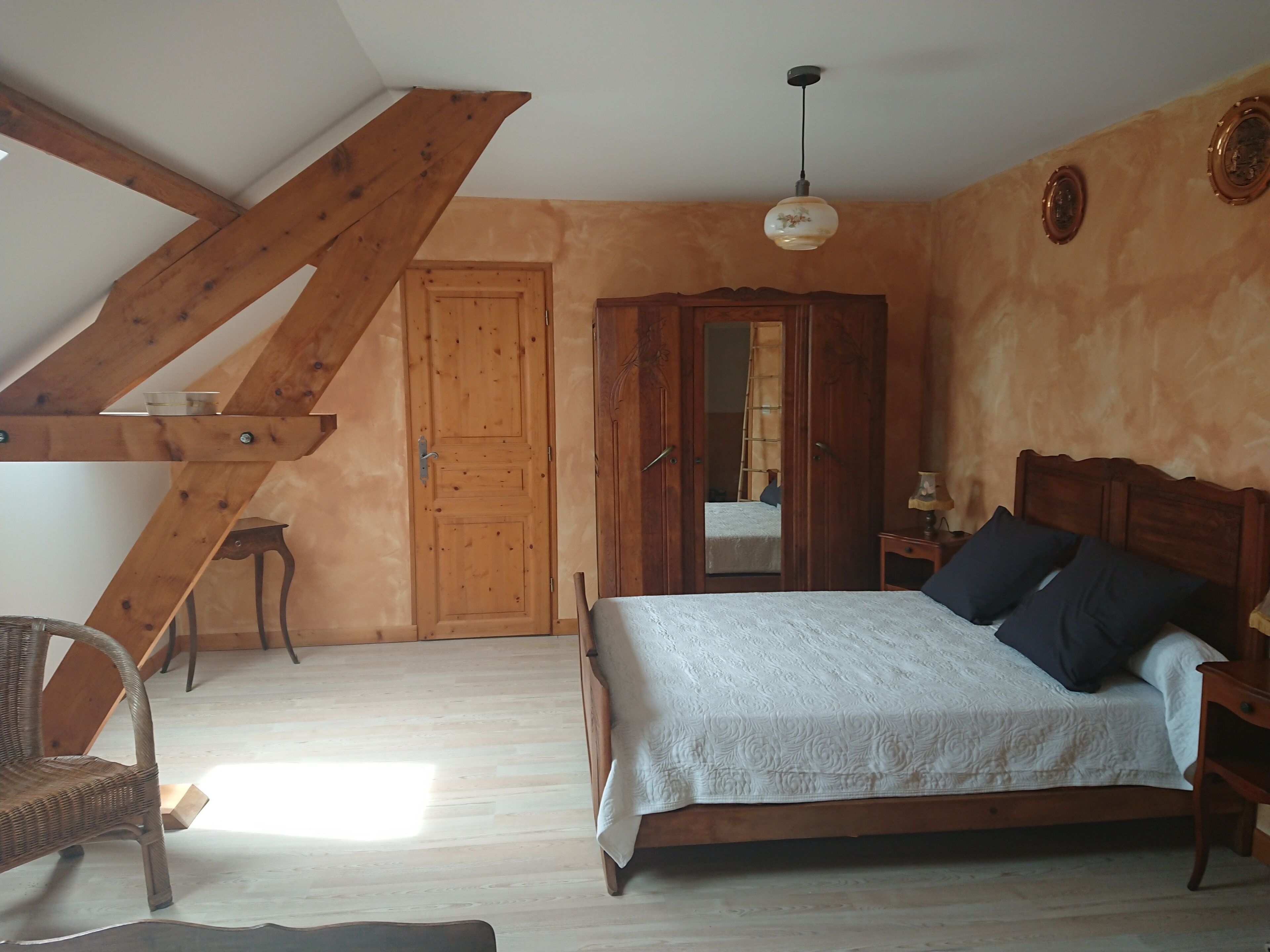Une chambre avec un lit en bois, une chaise, une armoire en bois et un plafond en pente.