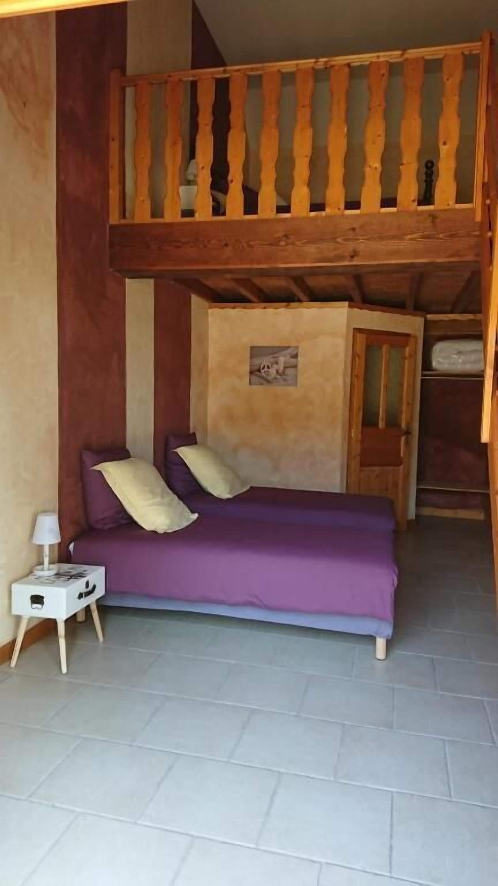 A room with a bunk bed, a small bedside table with a lamp, and a wall-mounted shelf.
