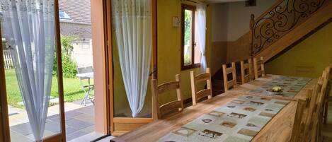 A dining area with a long wooden table, chairs, and a patterned tablecloth.