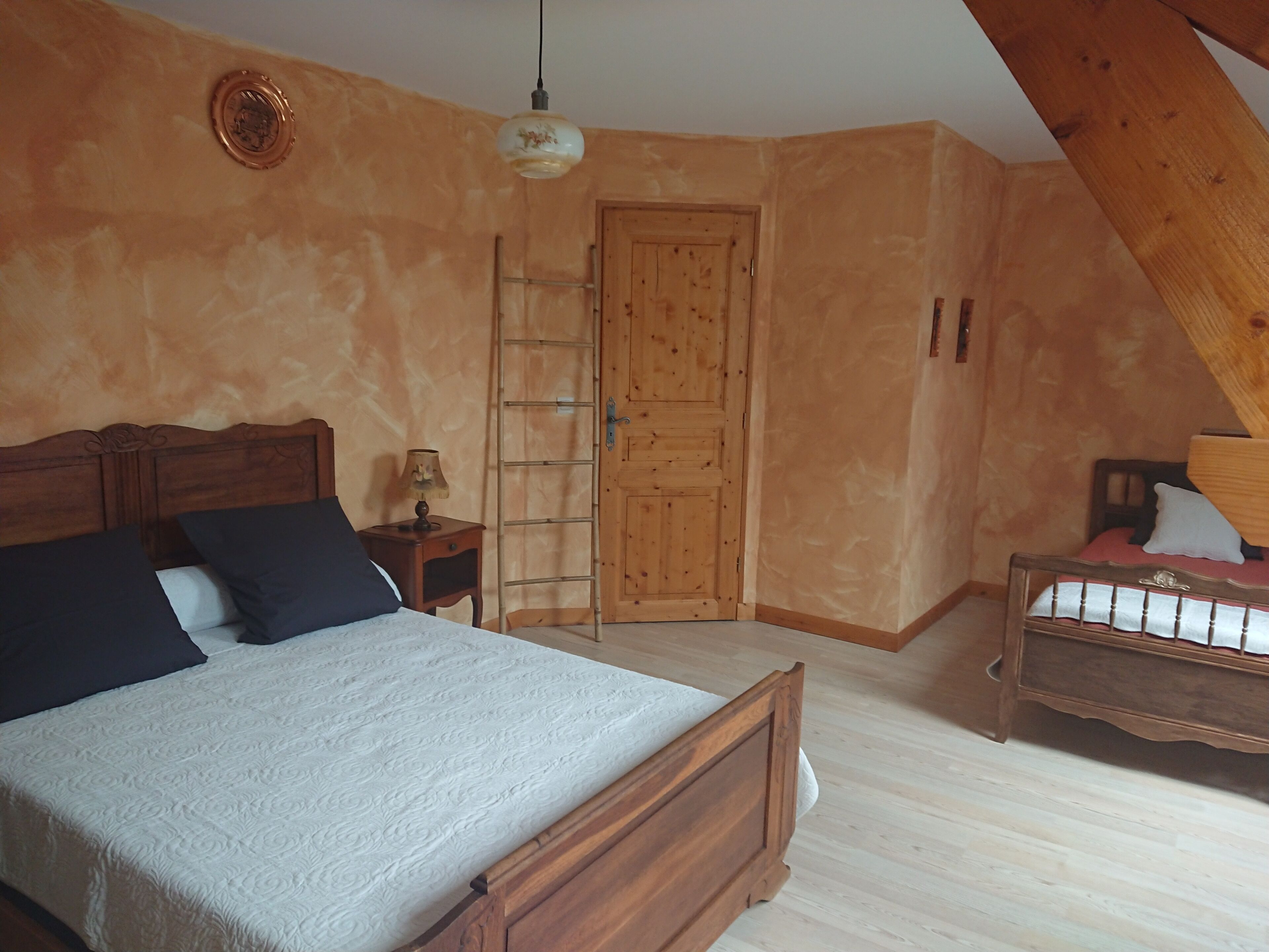 A bedroom with a wooden bed, a nightstand, a lamp, a wooden ladder, and a door.