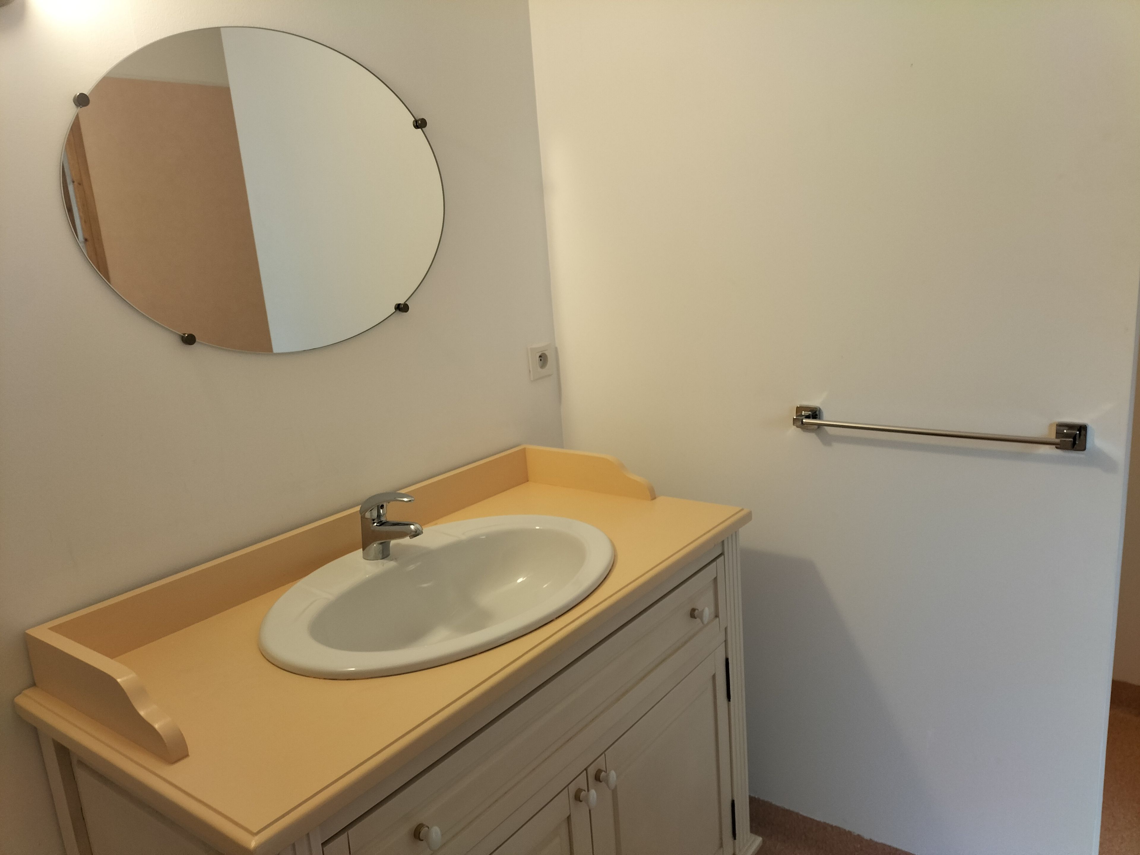 A bathroom with a round mirror, a sink, and a towel bar.