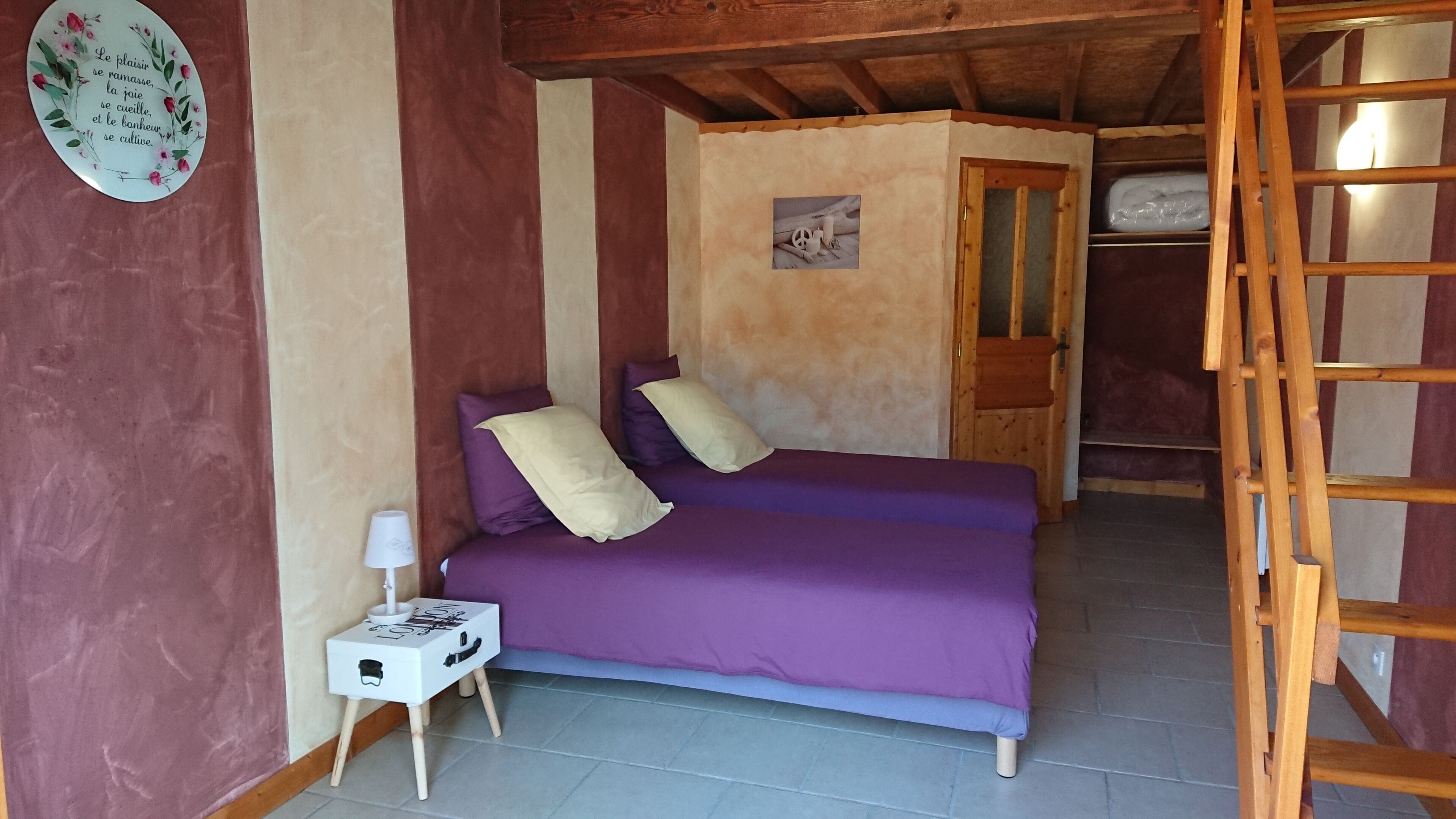 Une pièce comprenant un lit, une petite table de chevet, un élément de décoration murale et une échelle en bois.