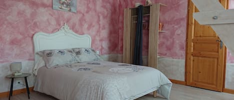 Un dormitorio con cama, mesita de noche, un cuadro, armario de madera y una puerta.