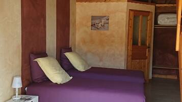 Ein Zimmer mit einem Etagenbett, einem Einzelbett mit violetter Bettwäsche, einem kleinen Nachttisch mit Lampe und einem an der Wand montierten Regal.