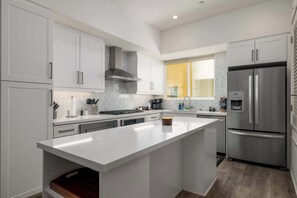 A modern kitchen with white cabinetry, a stainless steel refrigerator, and a large island. - NEW 3br Luxury Townhome | Gaslamp | Balboa Park (San Diego)