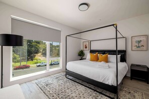 A modern bedroom with a four-poster bed, a large window, and a view of a street. - NEW 3br Luxury Townhome | Gaslamp | Balboa Park (San Diego)