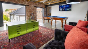 Una habitación amplia con mesa de billar, cómoda verde y alfombra roja estampada.