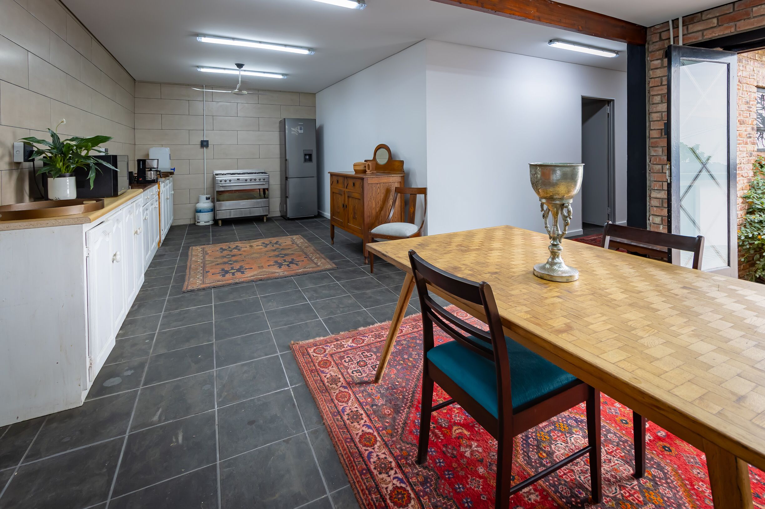 A kitchen with a dining area, featuring a wooden table, chairs, a refrigerator, a stove, and a cabinet.