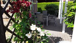 A garden with a trellis, white flowers, and a patio area with a table and chairs. - Spacious vacation home with 3 bedrooms, covered terrace, barbecue hut NaheOL (Hatten)