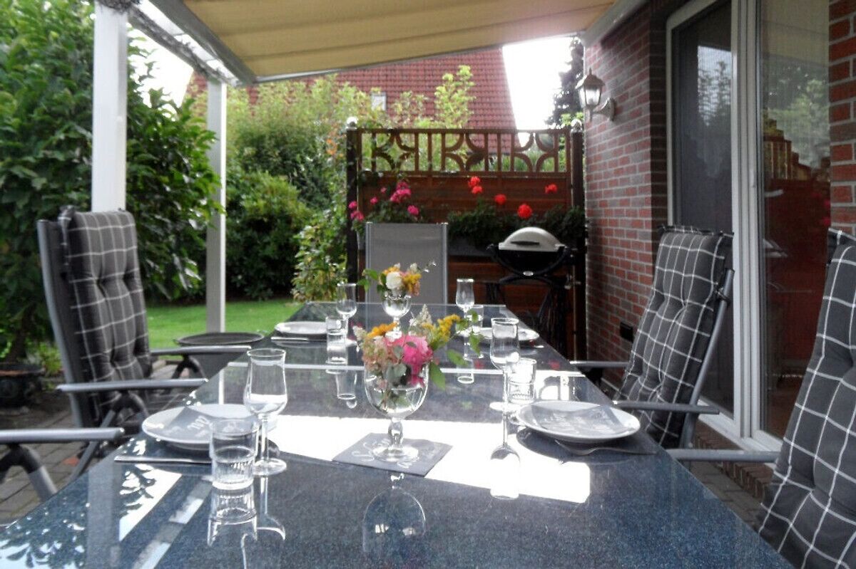 A patio table set for dining with chairs, a grill, and a garden view.