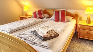 A double bed with two pillows, a bedside table with a lamp, and a blanket on the floor. - Spacious vacation home with 3 bedrooms, covered terrace, barbecue hut NaheOL (Hatten)