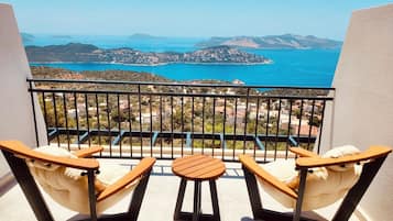 Varanda com duas cadeiras de madeira e uma pequena mesa, com vista para uma paisagem costeira com colinas e um corpo de água.