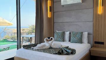 Una habitación de hotel moderna con una cama grande, vistas al exterior, aire acondicionado integrado y una mesita de noche.