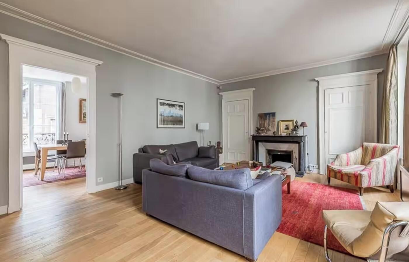 A spacious living room with a grey sofa, a red rug, and a fireplace.