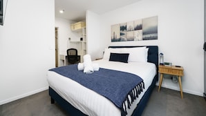 A modern hotel room with a large bed, a wooden nightstand, and a painting on the wall.