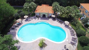 A swimming pool with lounge chairs and umbrellas, surrounded by palm trees and a building with a tiled roof. - Family Friendly 4Bd Townhome GameRoom near Disney 5149 (Kissimmee)