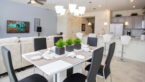 A dining area with a white table, black chairs, and potted plants. There is a ceiling fan, pendant lights, and a kitchen area in the background. - Family Friendly 4Bd Townhome GameRoom near Disney 5149 (Kissimmee)