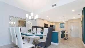 A modern kitchen with white cabinets, a central island, and a dining area with white chairs and a chandelier. - Lake View Resort Condo w Lazy River Near Disney (Kissimmee)