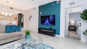 A modern living room with a teal accent wall, a flat-screen TV, a glass coffee table, and a sofa with blue cushions. - Lake View Resort Condo w Lazy River Near Disney (Kissimmee)