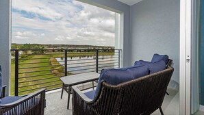 A balcony with wicker furniture, a table, and a view of a golf course and water. - Lake View Resort Condo w Lazy River Near Disney (Kissimmee)