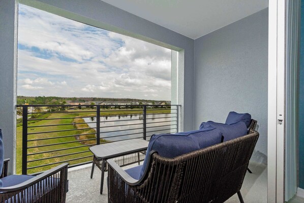 A balcony with wicker furniture, a table, and a view of a golf course and water.