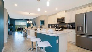 A modern kitchen with white cabinets, stainless steel appliances, and a central island with bar stools. - Lake View Resort Condo w Lazy River Near Disney (Kissimmee)