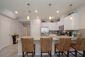 A modern kitchen with white cabinets, a stainless steel refrigerator, and a bar area with patterned chairs. - Modern 4BR w Patio & Resort Pool Compass Bay 5102 (Kissimmee)