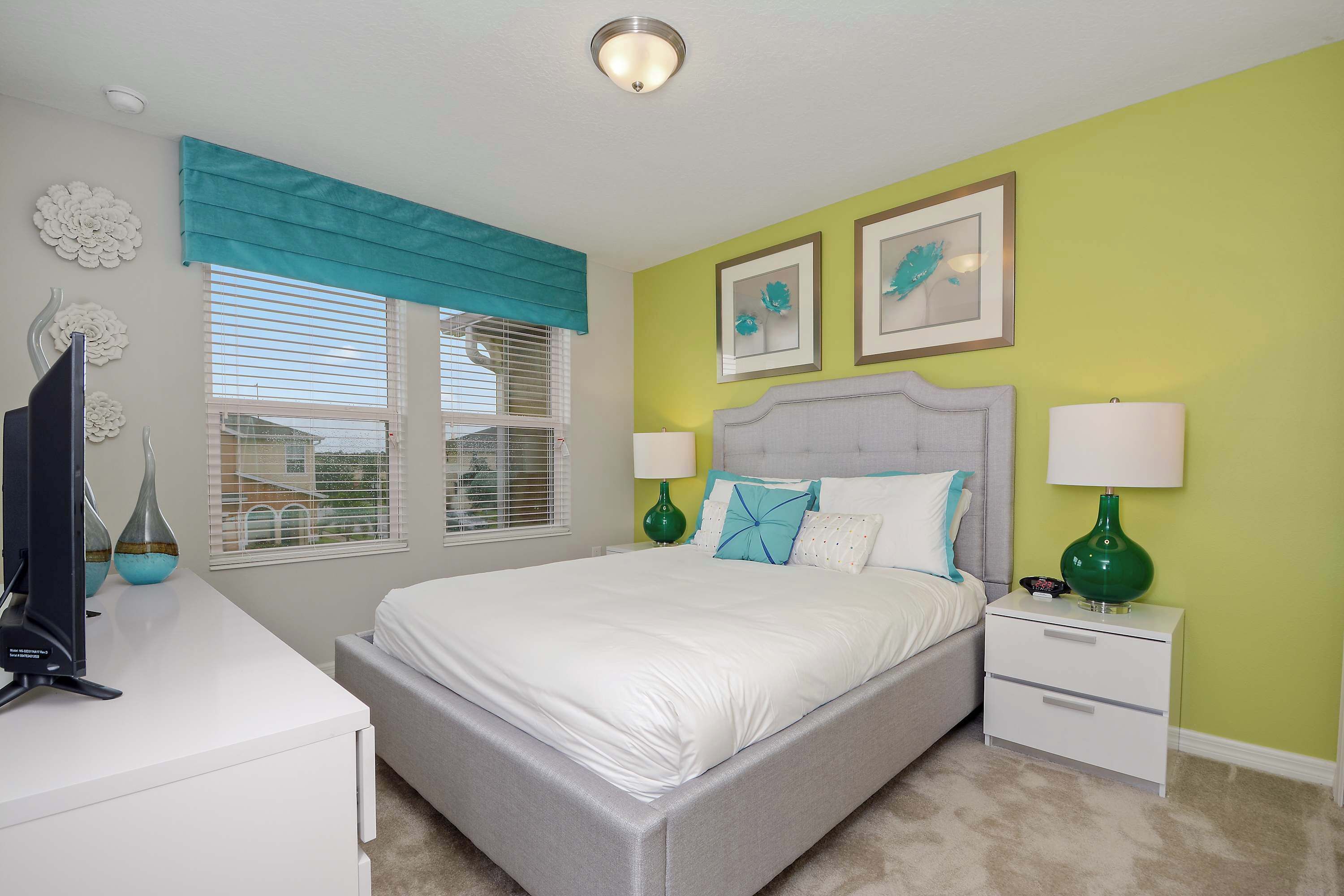A bedroom with a bed, bedside tables, a TV, and decorative items.