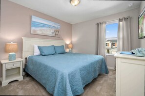 Een slaapkamer met een groot bed, een nachtkastje met lamp, een kapstok en een raam met gordijnen.