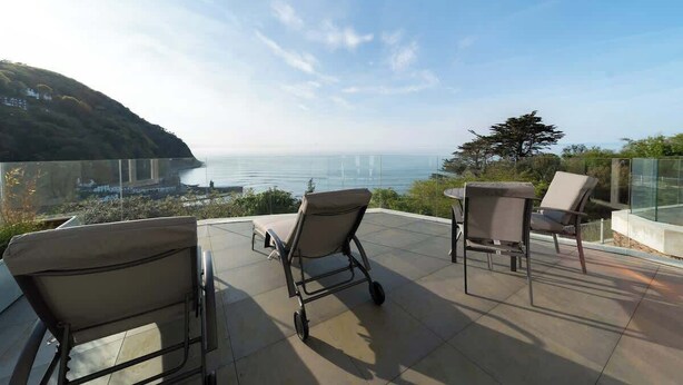 A terrace with three chairs and a table, overlooking a scenic view of the sea and a hilly landscape. - Romantic Sea View Escape at Tors Park - Terrace (Lynmouth)