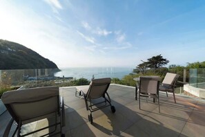 Una terrazza con tre sedie e un tavolo, che si affaccia su un panorama mozzafiato di mare e un paesaggio collinare.
