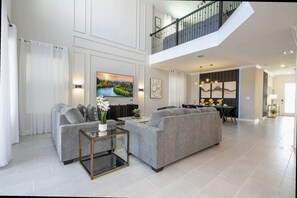 Ein geräumiges Wohnzimmer mit einer grauen Sofagarnitur, einem Glastisch und einem Landschaftsbild.