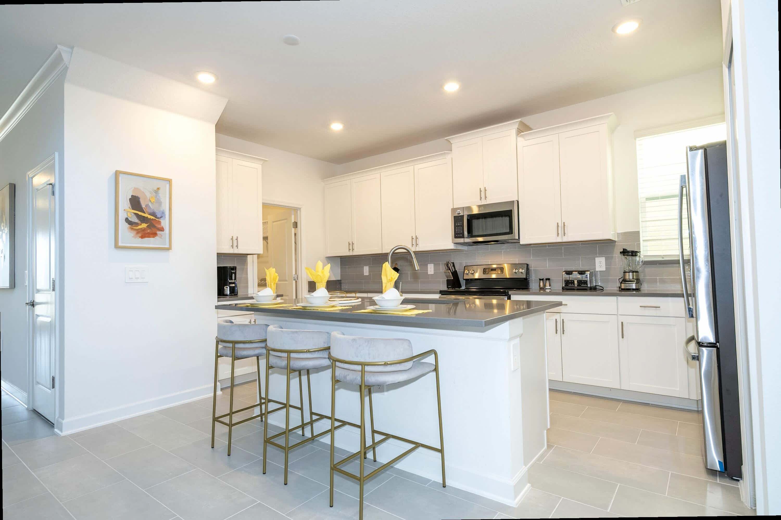 A modern kitchen with white cabinets, a central island with bar stools, stainless steel appliances, and a large refrigerator.