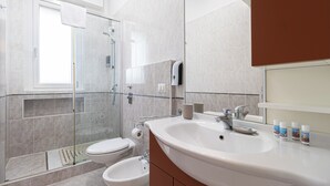 A modern bathroom with a glass-enclosed shower, a toilet, a sink with a mirror, and toiletries on the counter. - Italianway Comfort - Rembrandt 58 (Milan)