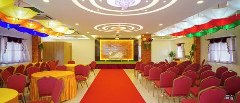 A conference room with a red carpet, rows of red chairs, and tables with yellow tablecloths.