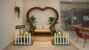 A reception area with a heart-shaped wall decoration, a sofa, potted plants, a 'Photo Corner' sign, and a glass door with a sign reading "BHADRACHALAM BAHU". - Bhadrachalam Nest Inn (Mysore)