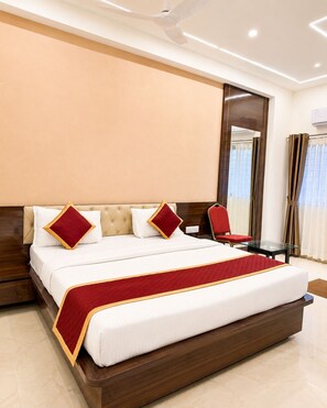 A hotel room with a large bed, a wooden headboard, a red and white bedspread, and a glass table with a chair. - Bhadrachalam Nest Inn (Mysore)