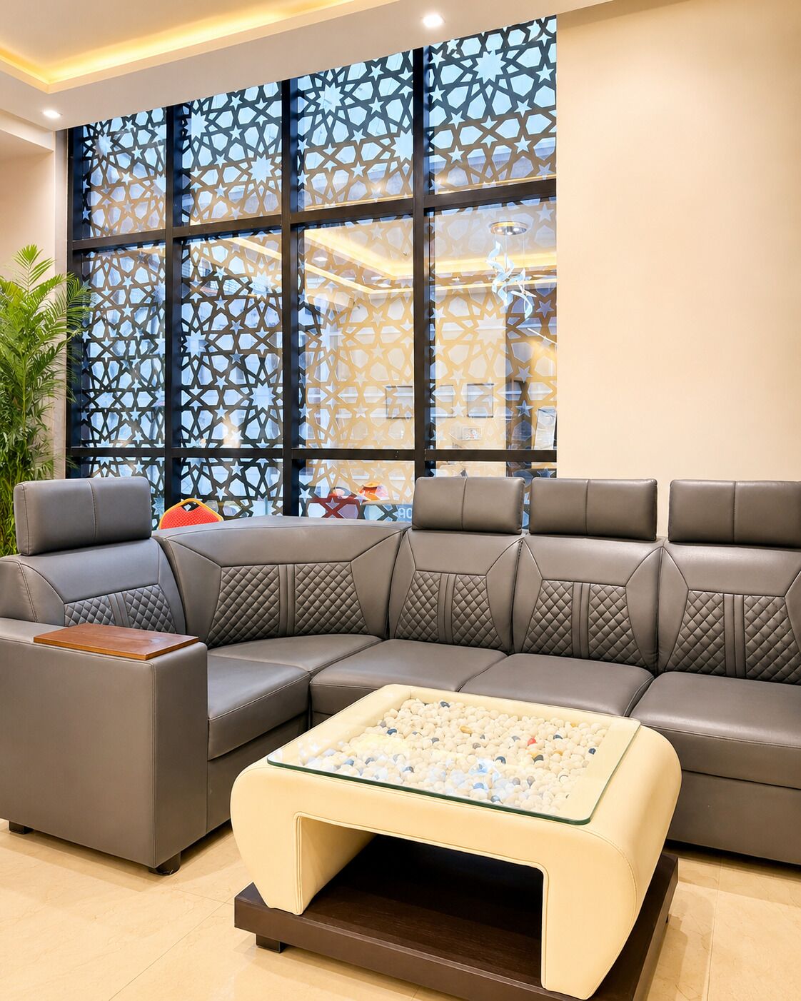 A modern living room with a sectional sofa, a glass coffee table, and a decorative screen with geometric patterns.