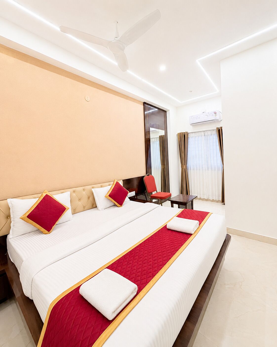 Une chambre d’hôtel avec un grand lit, un bureau, une chaise, un miroir et un ventilateur de plafond.