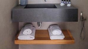 A modern bathroom with a large mirror, a built-in sink, and a wooden shelf holding towels.