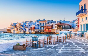 A coastal town with buildings along the waterfront, stone-paved walkways, and outdoor seating areas.