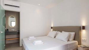 A modern bedroom with a large bed, a bedside lamp, and a wall-mounted air conditioner.