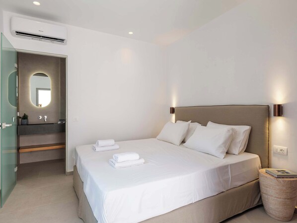 A modern bedroom with a large bed, a bedside lamp, and a wall-mounted air conditioner.
