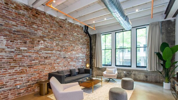 A modern living room with a brick wall, a sofa, a coffee table, and a large window with curtains. - Inventors` Loft - Luxury, Upscale, Quiet 2BD! (Philadelphia)